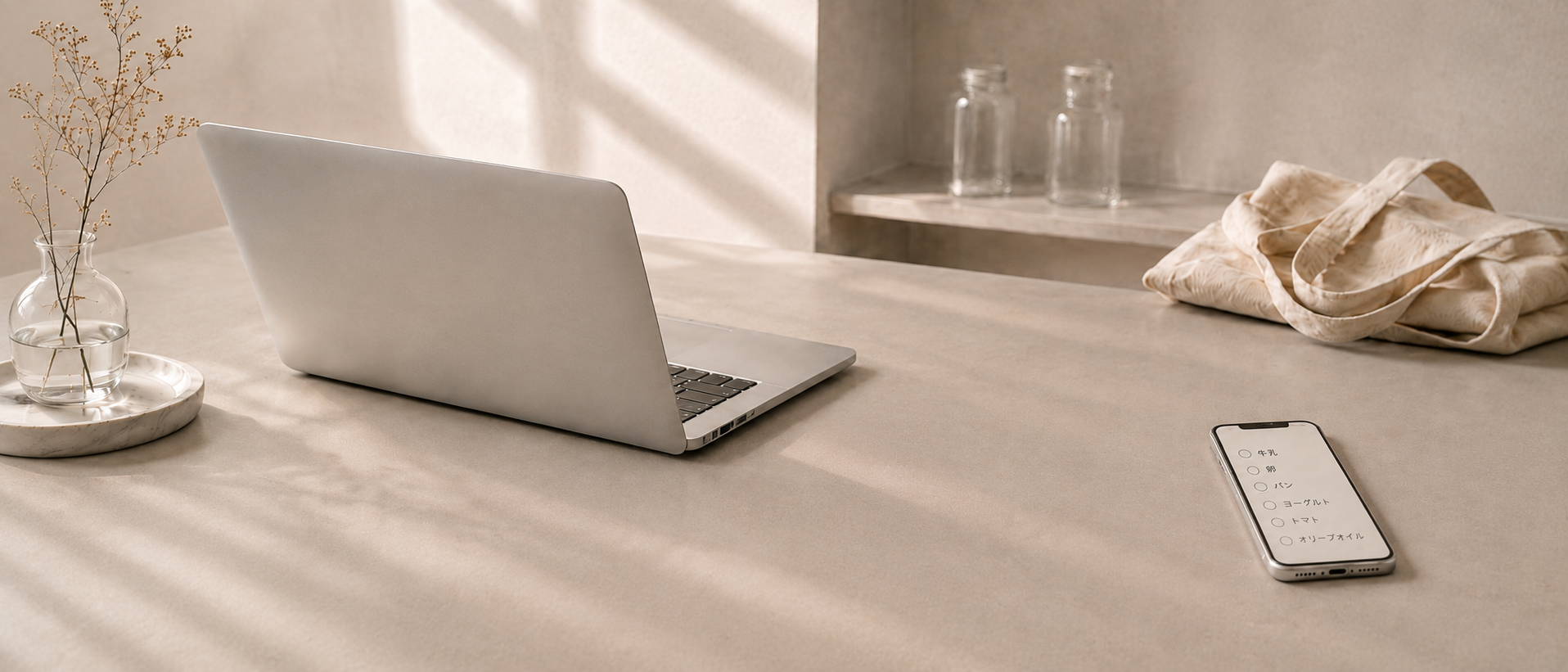 淡い自然光の机に置かれたラップトップと、買い物リストを表示したスマートフォン